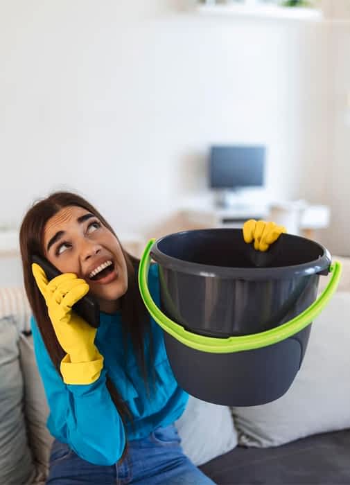 Water Damage Restoration Contractor New York - A Woman Holding a Bucket Catching Water from a Leak